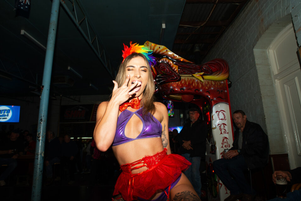 Performer in a rainbow feathered headpiece and colourful skimpy outfit blows a kiss during a lively performance at a WA pub.